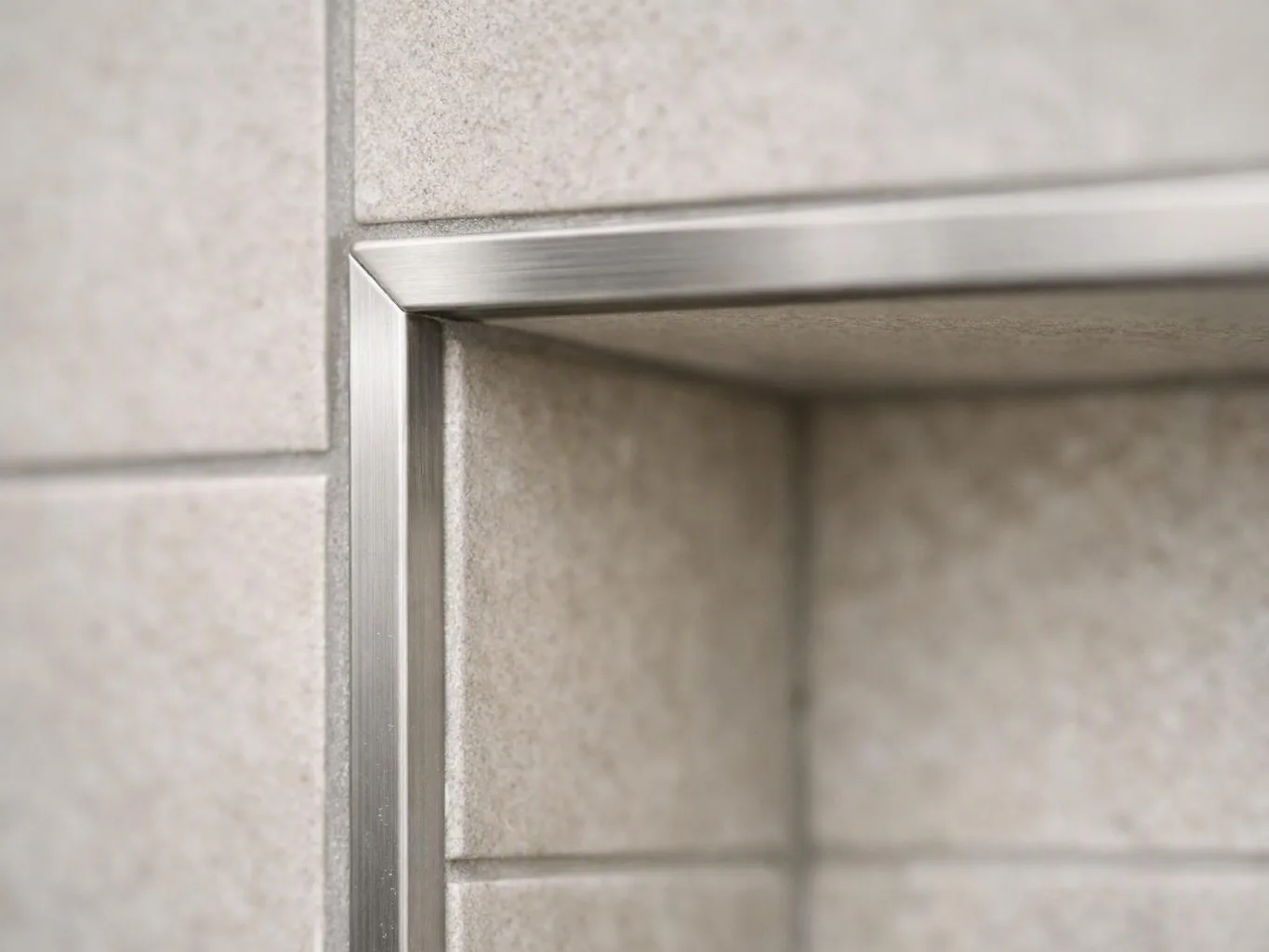 Close-up of a brushed metal frame around a beige tiled shower niche wall
