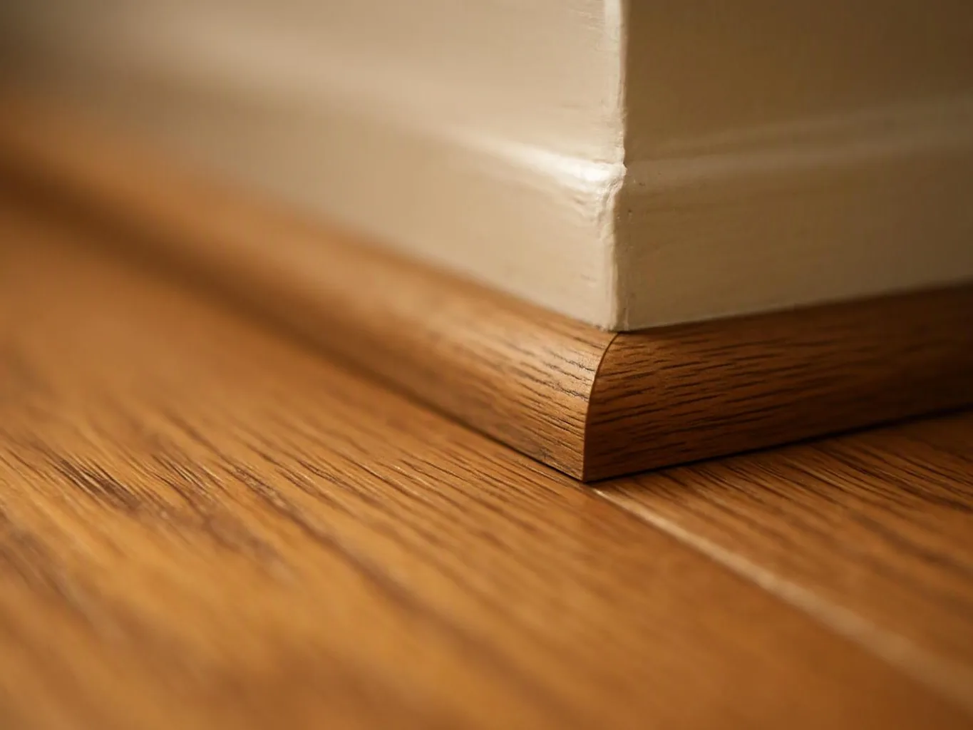 Close-up of a white wall baseboard meeting a polished wooden floor at a corner