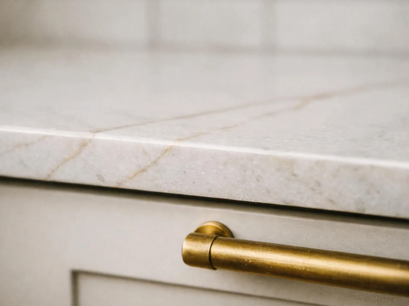 A gold cabinet handle sits below a light marble countertop with faint veining