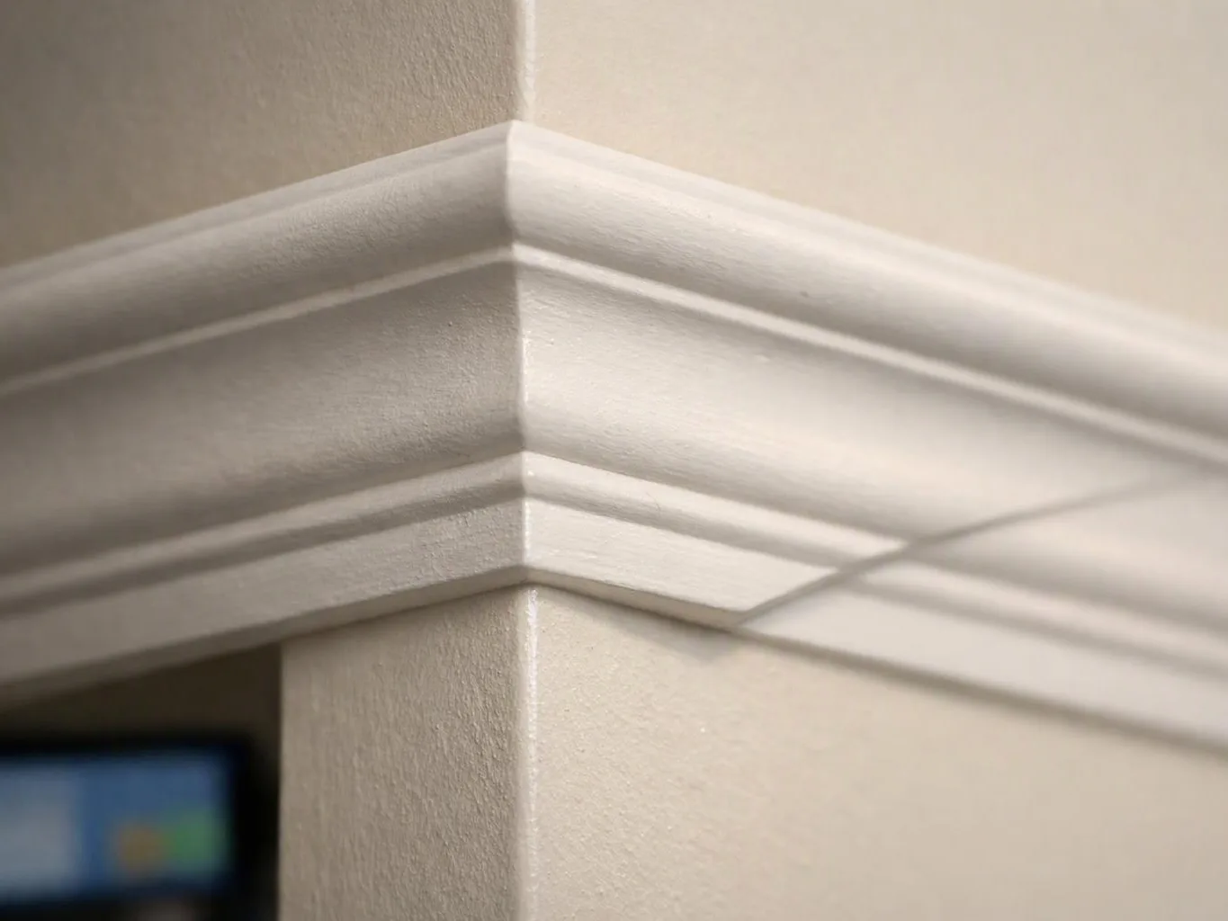 White crown molding wraps an interior wall corner with sunlight casting long shadows across the paint